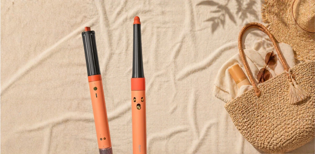 Dyson Airwrap na bež ljetnom peškiru uz pletenu torbu i sunčane naočale.